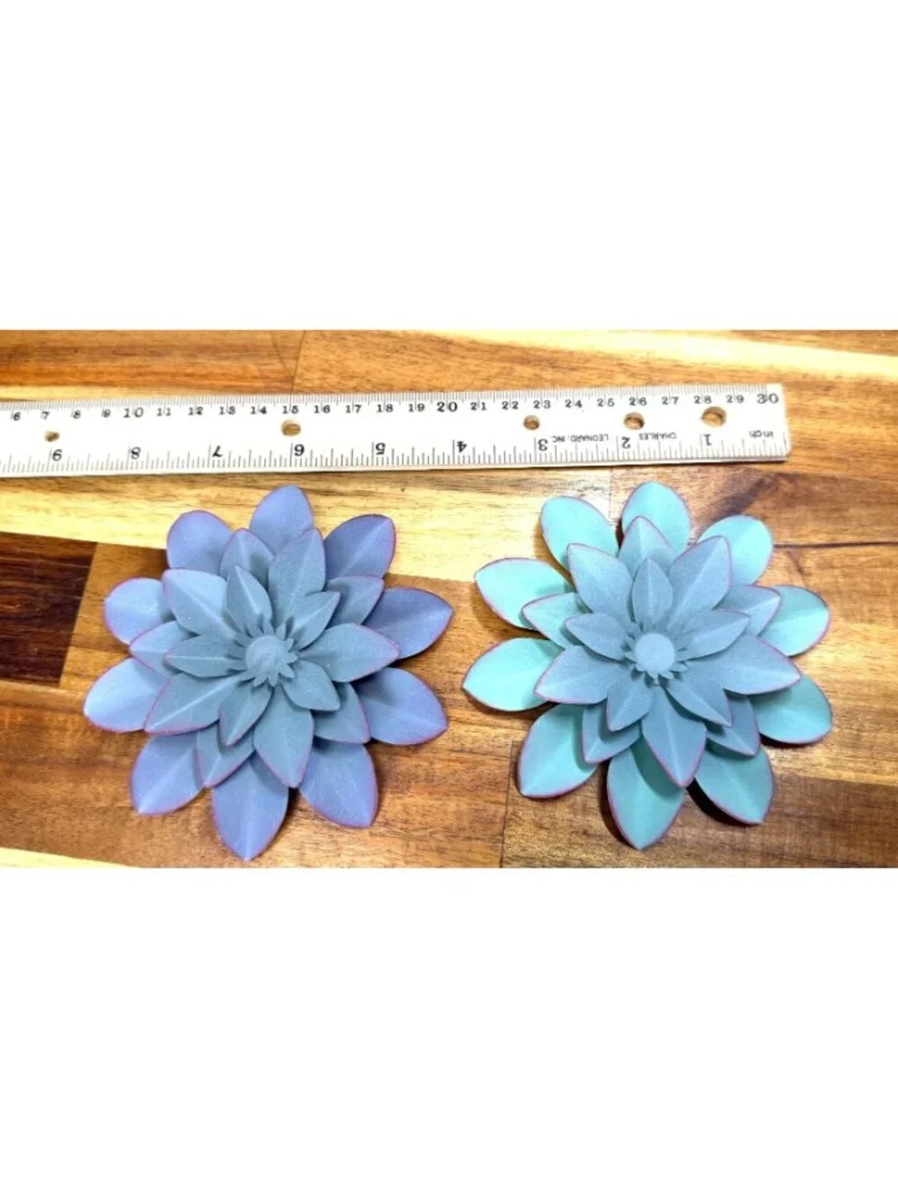 Small, teal-colored metal wall art feature is a layered flower design with disti